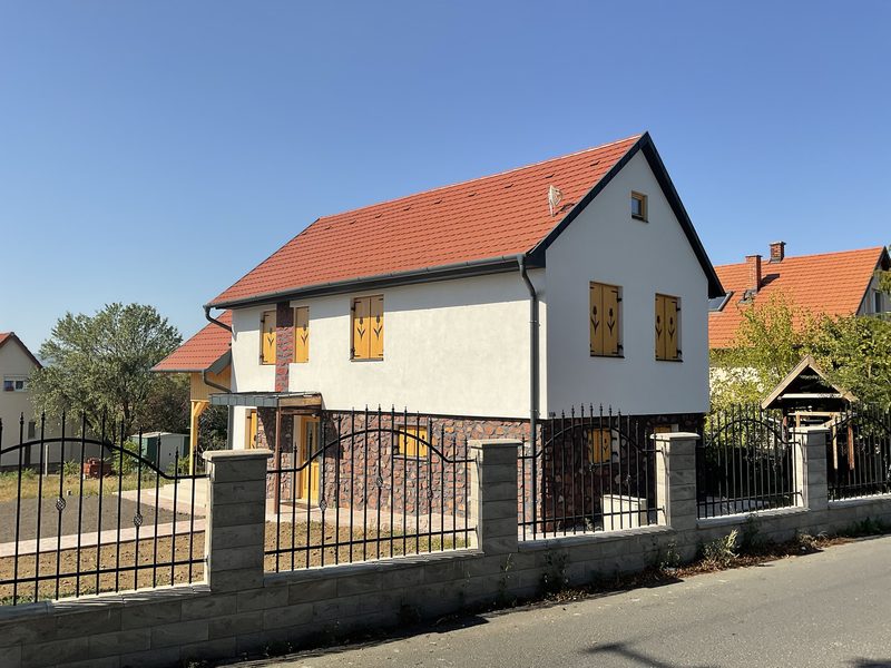 Stone-faced plinth, timber shutters with a tulip motif and a tiled roof.