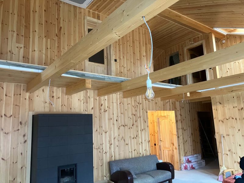 Holzverkleideter Innenraum mit sichtbaren Balken und Kamin.