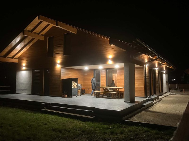 Die überdachte Terrasse am Abend mit beleuchteter Fassade.